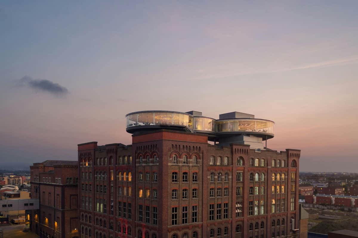 A historic brick building with a modern circular glass structure on the roof, viewed during sunset.