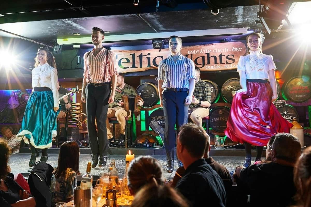 Dublin: Celtic Nights with Irish Dinner, Music & Dance Show Performers in traditional Irish attire dancing on a stage with musicians in the background and an audience watching.