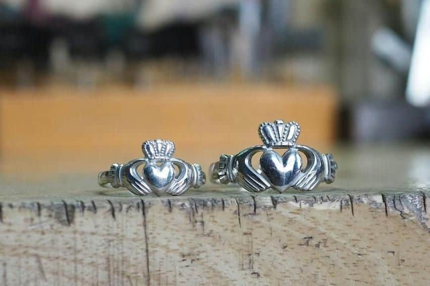 Dublin: Forge a Claddagh Ring Two silver Claddagh rings with heart, crown, and hands designs displayed on a wooden surface.