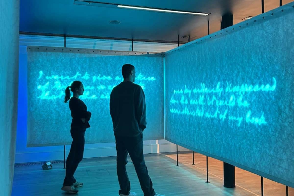 Deux personnes se tiennent dans une pièce faiblement éclairée et regardent un texte bleu lumineux affiché sur des panneaux translucides.