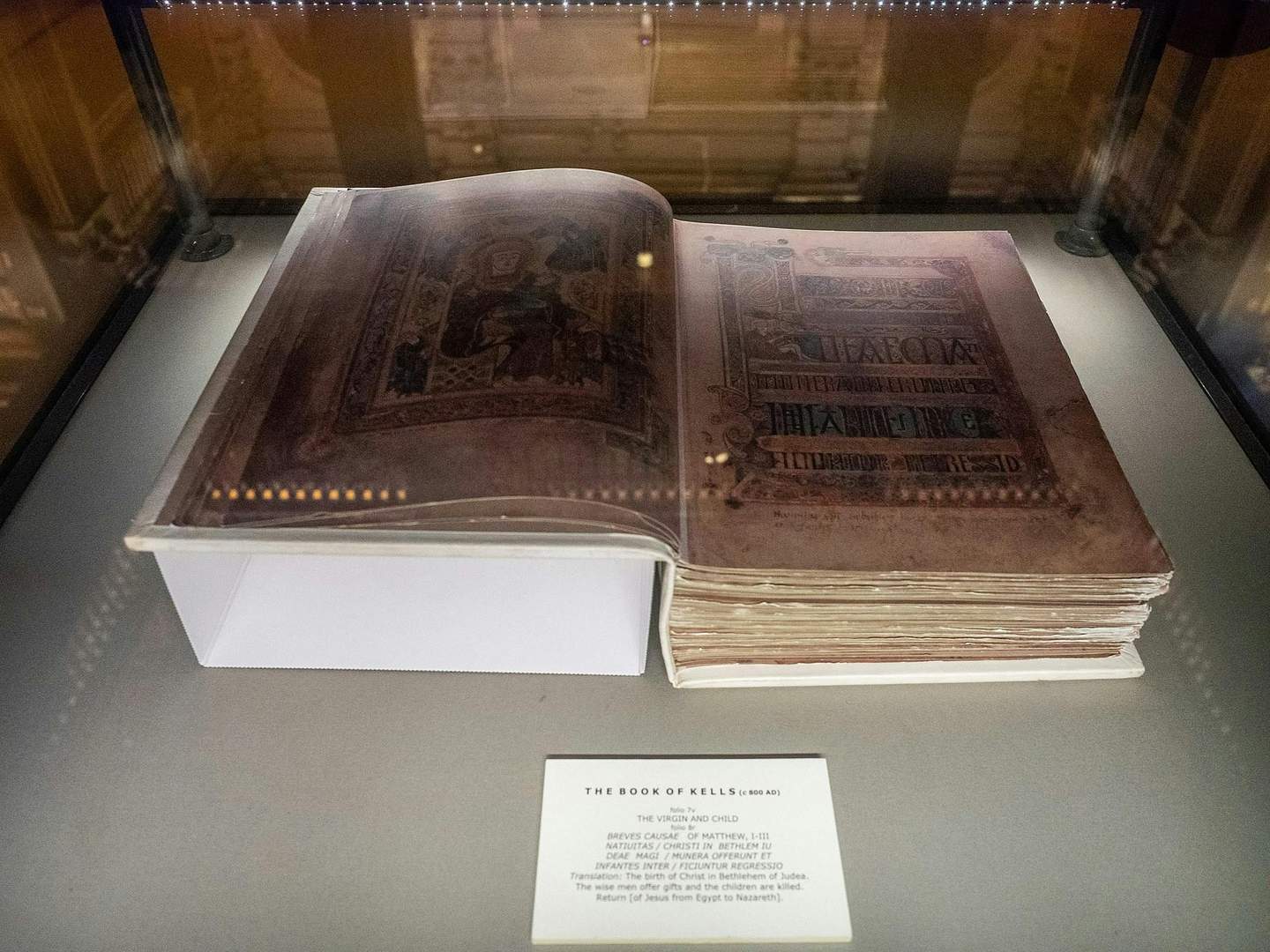 Un manuscrito iluminado, "El Libro de Kells", expuesto en una vitrina con una placa descriptiva debajo.
